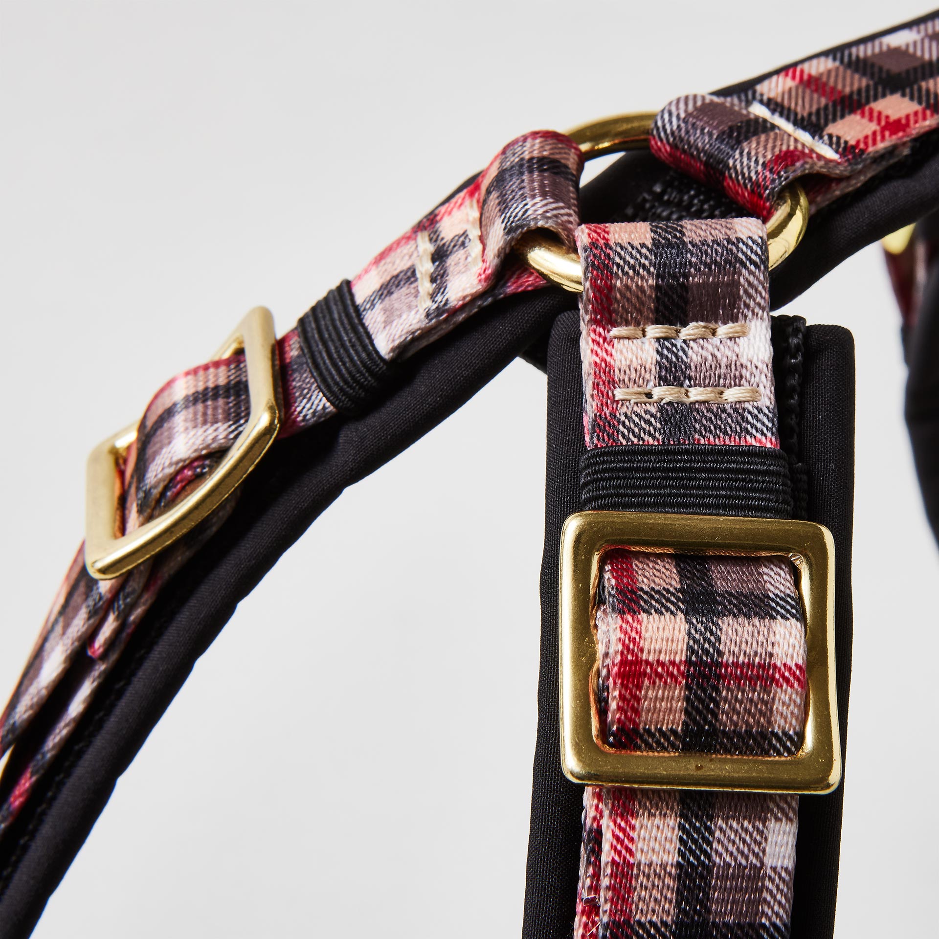 Detail verstellbares gepolstertes Hundegeschirr „Flaneur“ mit goldfarbenem Gurtbandschieber zur Größenanpassung und Karomuster in Schwarz, Beige und Rot.