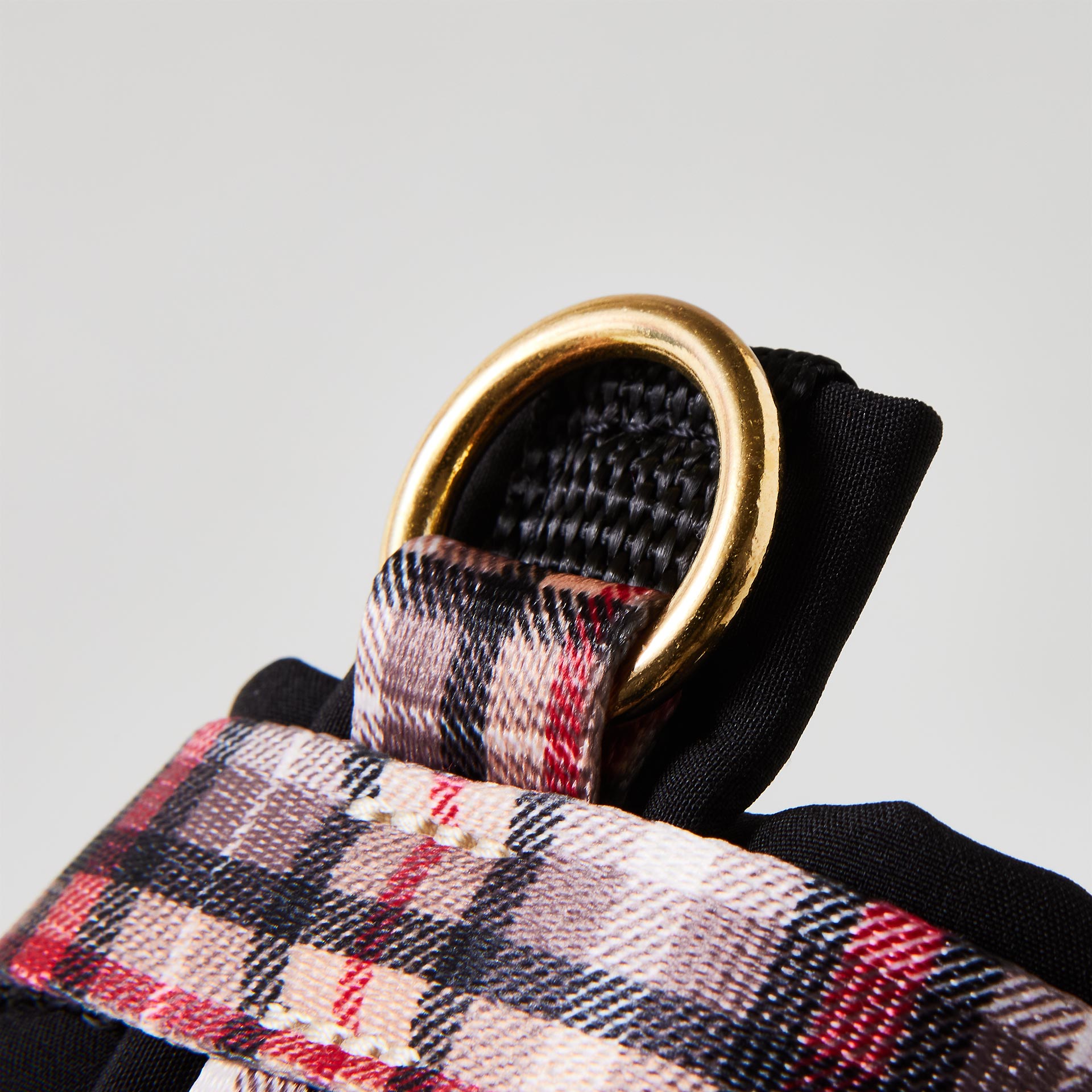 Nahaufnahme verstellbares Hundegeschirr „Flaneur“ mit gepolstertem goldfarbenem O-Ring zum Einhaken des Karabiners und Karomuster in Schwarz, Beige und Rot.