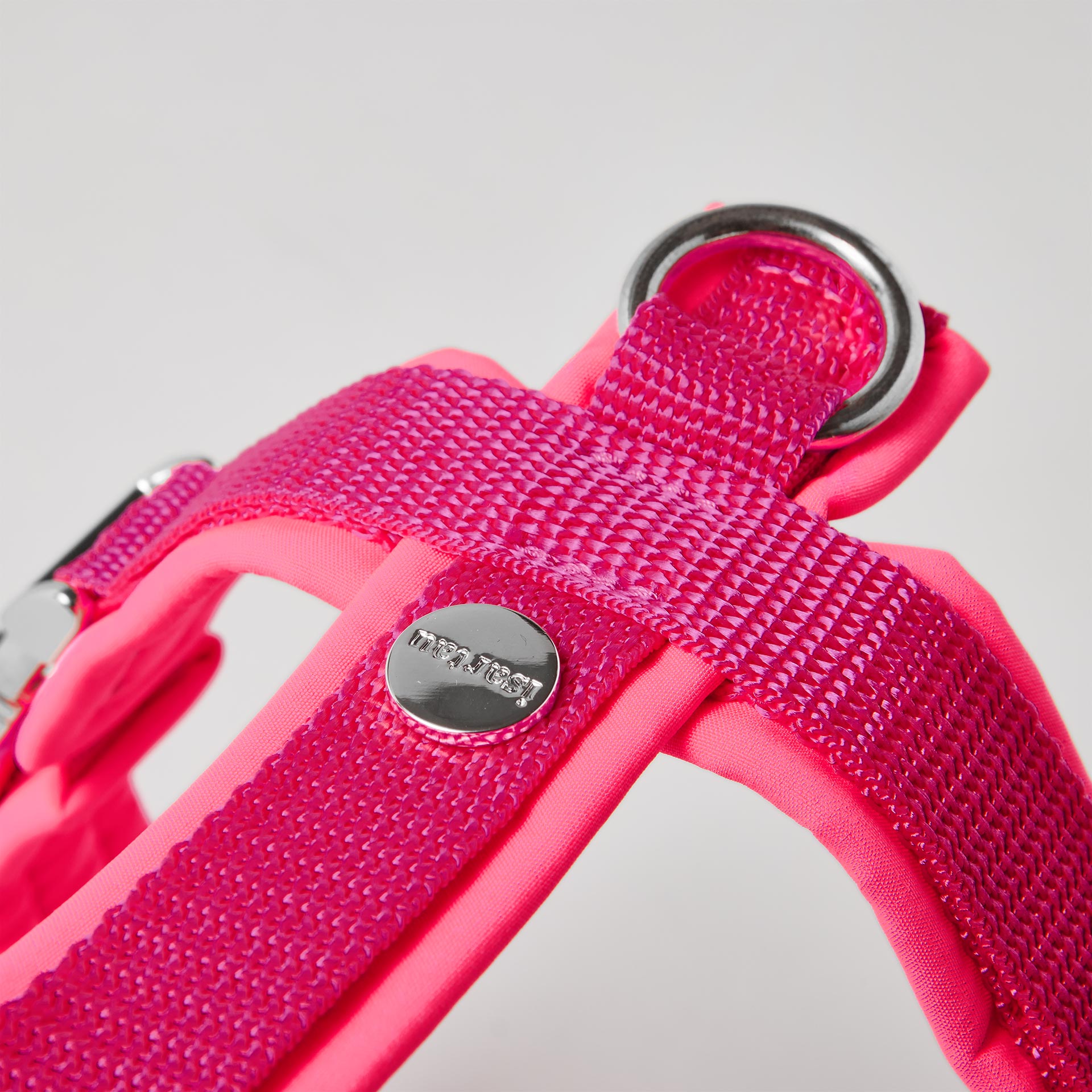 Rückenstück des neonpinken Hundegeschirrs mit gepolstertem O-Ring zum Einhaken des Karabiners und Logo-Niete
