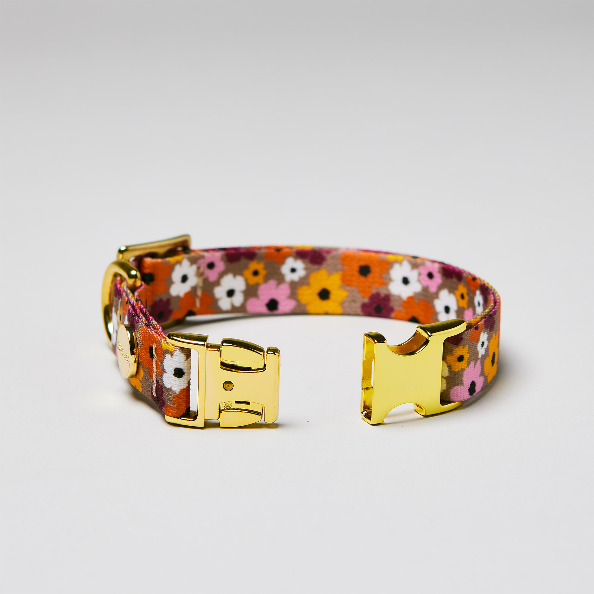 Detailaufnahme verstellbares Welpenhalsband „Blumenmeer“ mit offener goldfarbener Steckschließe, Gurtband mit Blumenprint.
