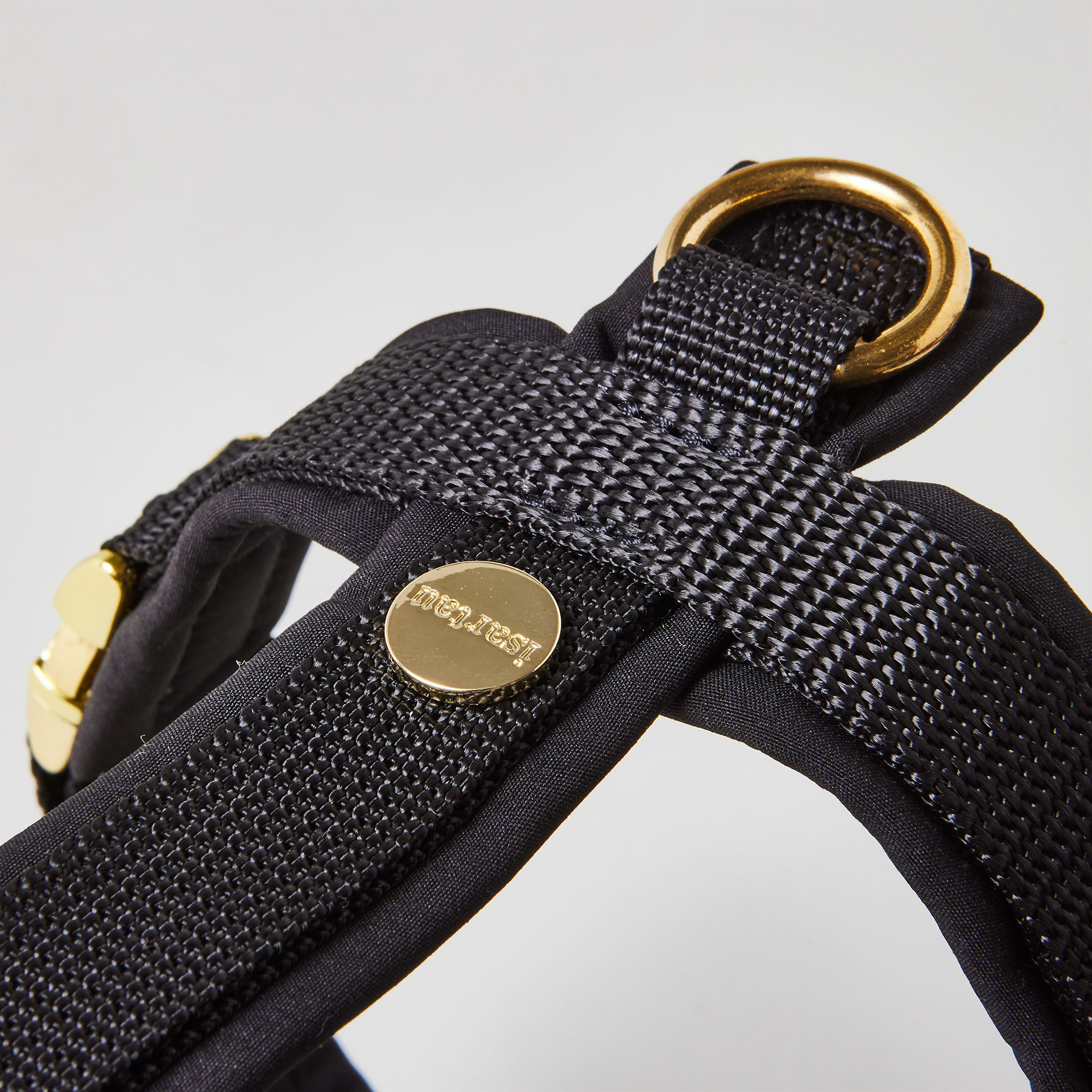 Rückenstück des schwarzen Hundegeschirrs mit goldfarbenem O-Ring und Logo-Niete