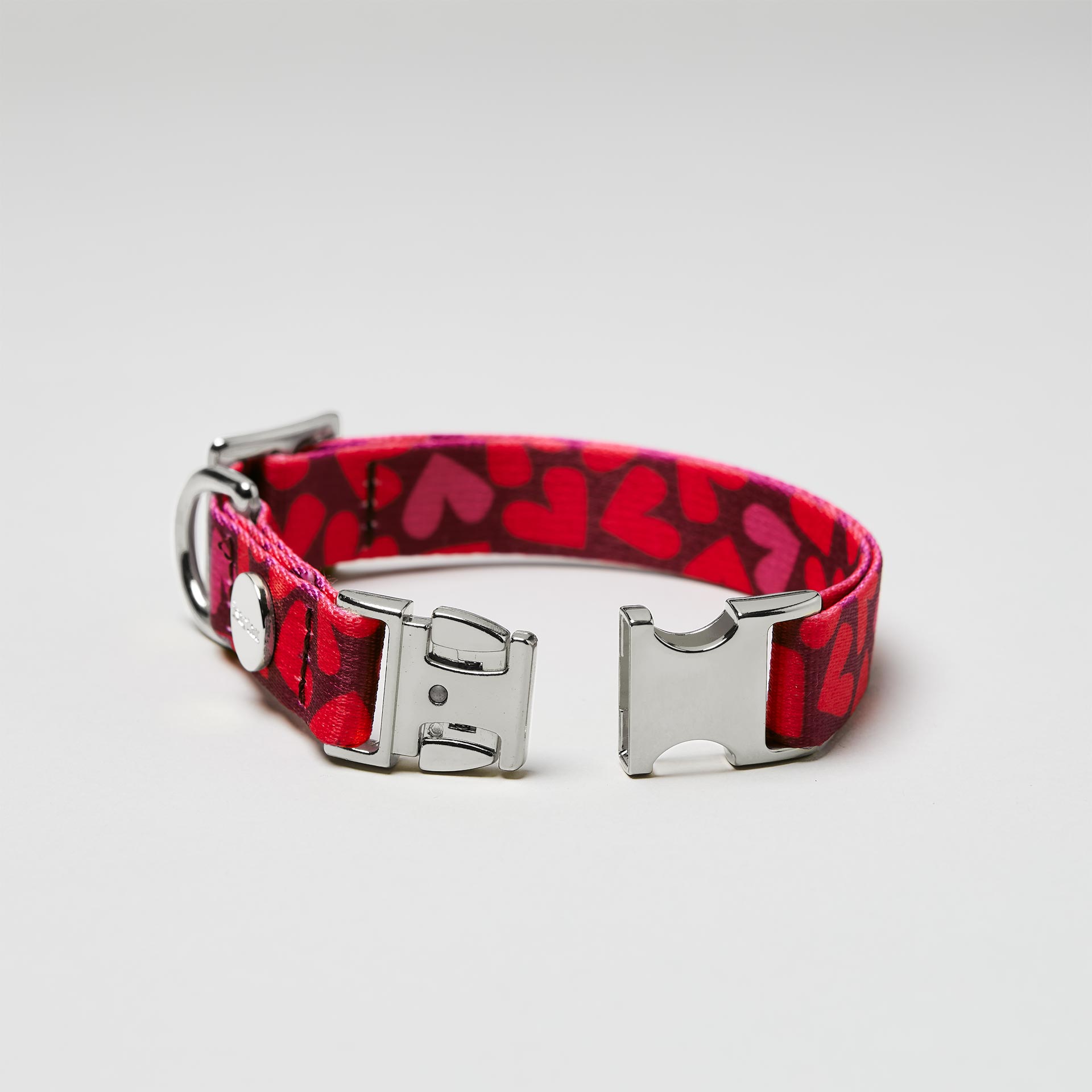 Detailaufnahme verstellbares Welpenhalsband Herzklopfen mit offener silberfarbener Steckschließe, Gurtband mit Herzmotiv in Rottönen