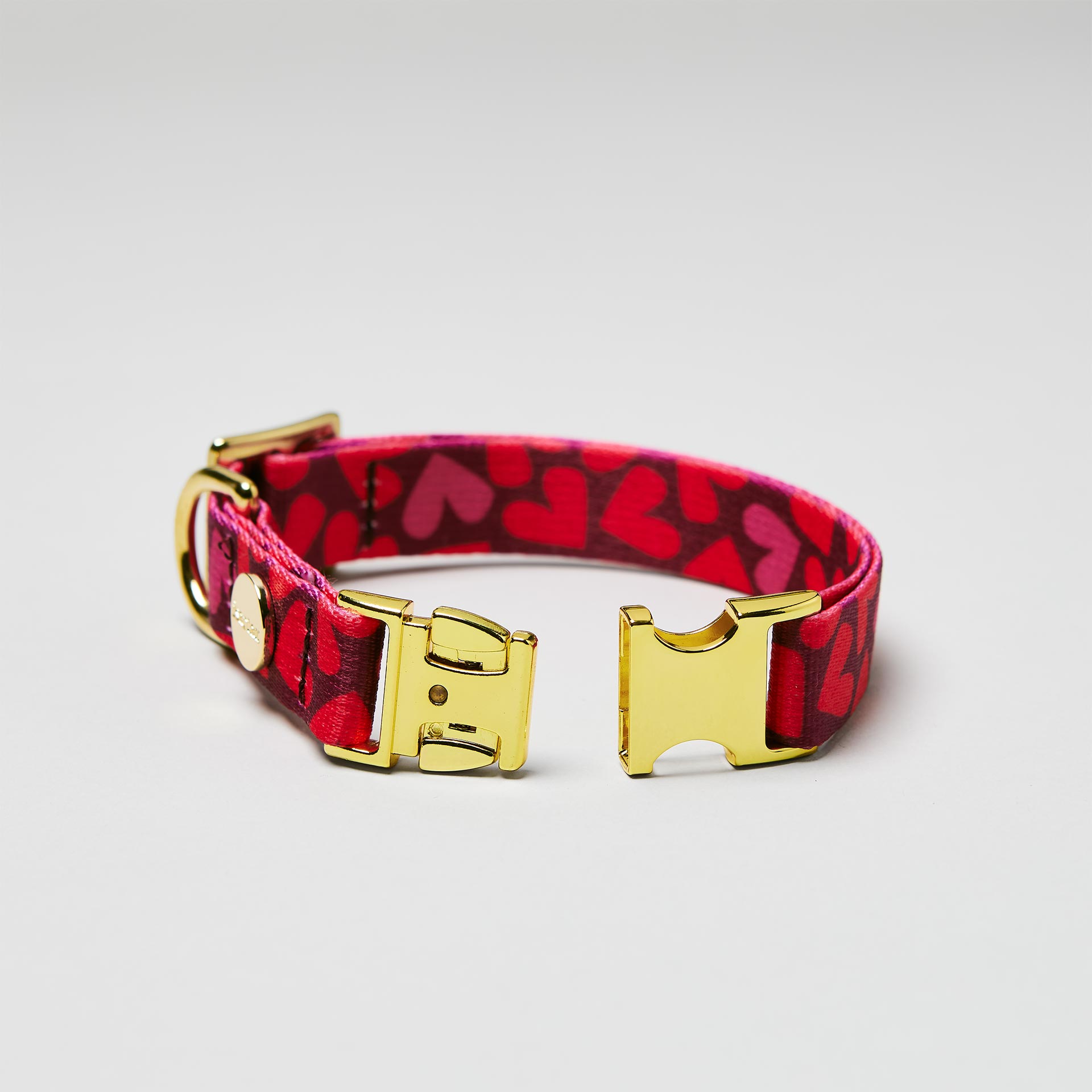Detailaufnahme verstellbares Welpenhalsband Herzklopfen mit offener goldfarbener Steckschließe, Gurtband mit Herzmotiv in Rottönen
