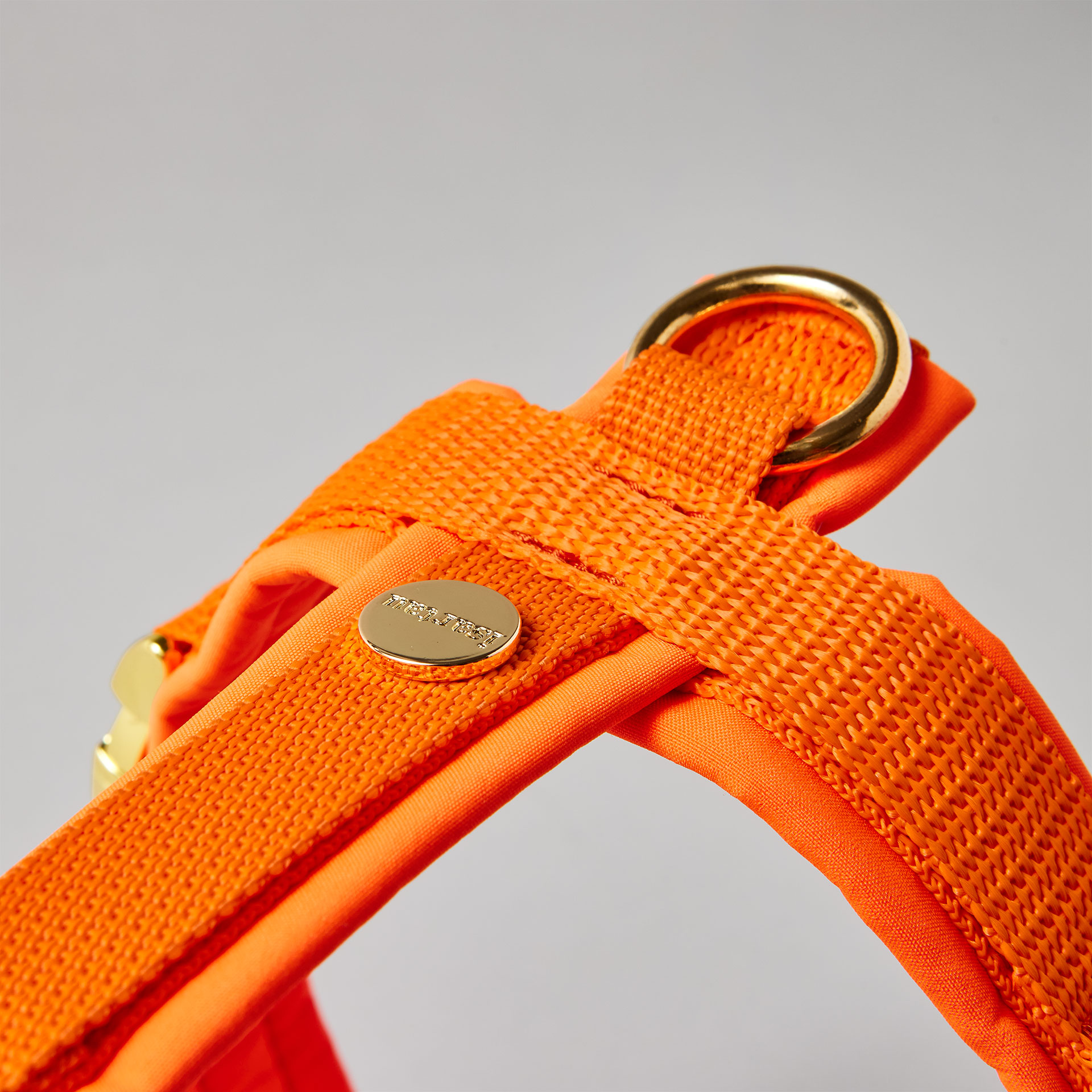 Rückenstück des neonorangen Hundegeschirrs mit goldfarbenem O-Ring und Logo-Niete